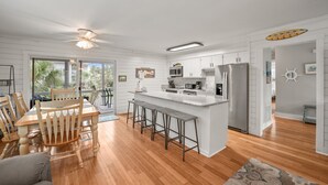 A modern kitchen with white cabinetry, a central island with bar stools, and a dining area with wooden chairs.