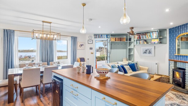 A modern kitchen with a wooden island, blue cabinets, and a view of the sea. - A Coastal Haven at 2 Harbour View (Roundstone)