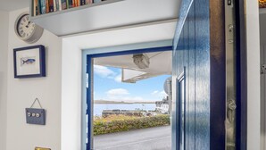 A door with a view of a coastal road and buildings. - A Coastal Haven at 2 Harbour View (Roundstone)
