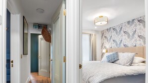 A bedroom with a bed, a patterned wall, a hanging light fixture, and a door leading to another room. - A Coastal Haven at 2 Harbour View (Roundstone)