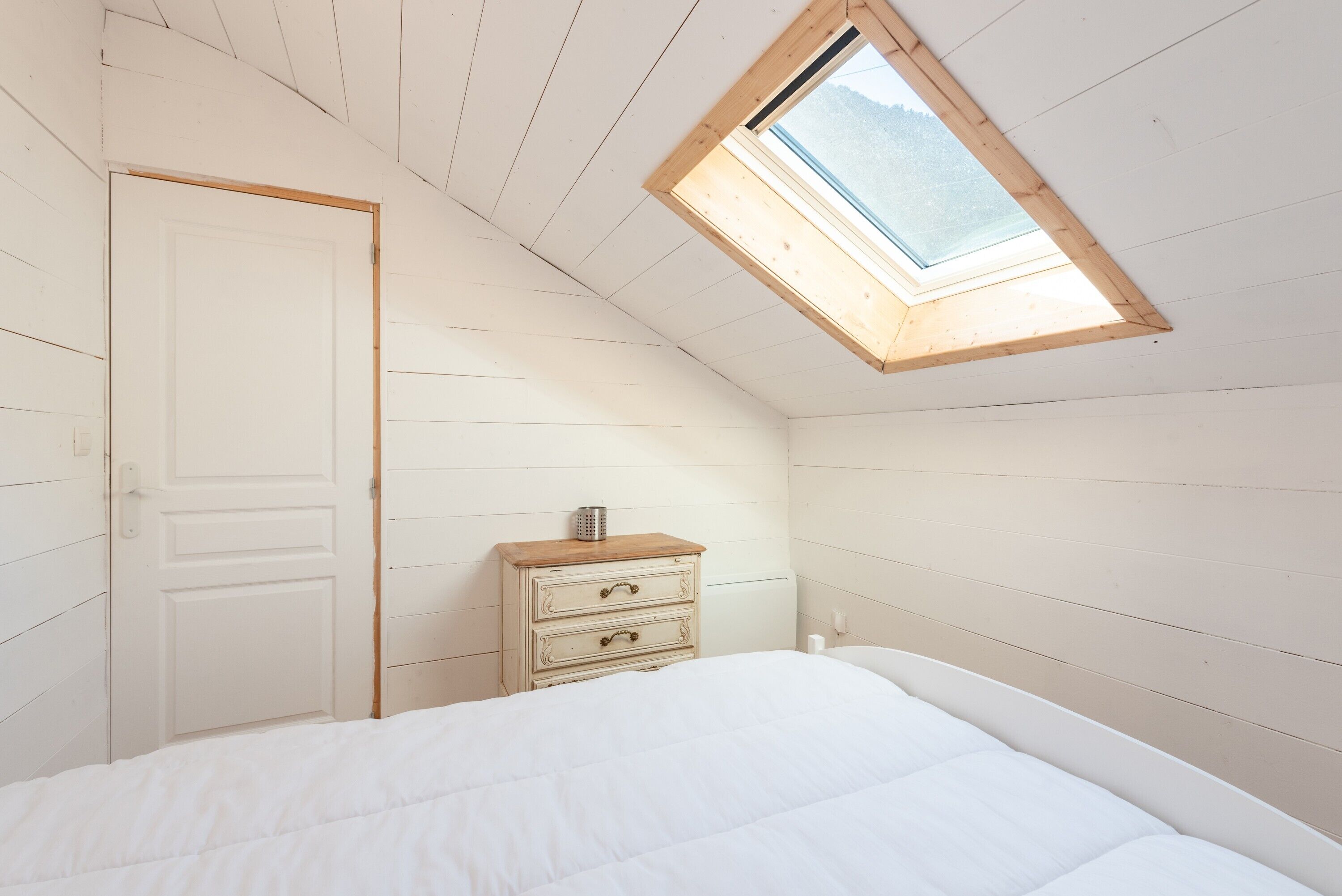 Un dormitorio con tragaluces, una puerta blanca, un aparador de madera y una cama.
