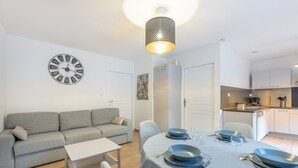 Una sala de estar moderna con un sofá, una mesa de comedor preparada para cuatro comensales y una cocina al fondo.