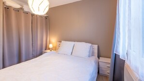 Un dormitorio con cama, cortinas, una lámpara de noche y una lámpara de pared.