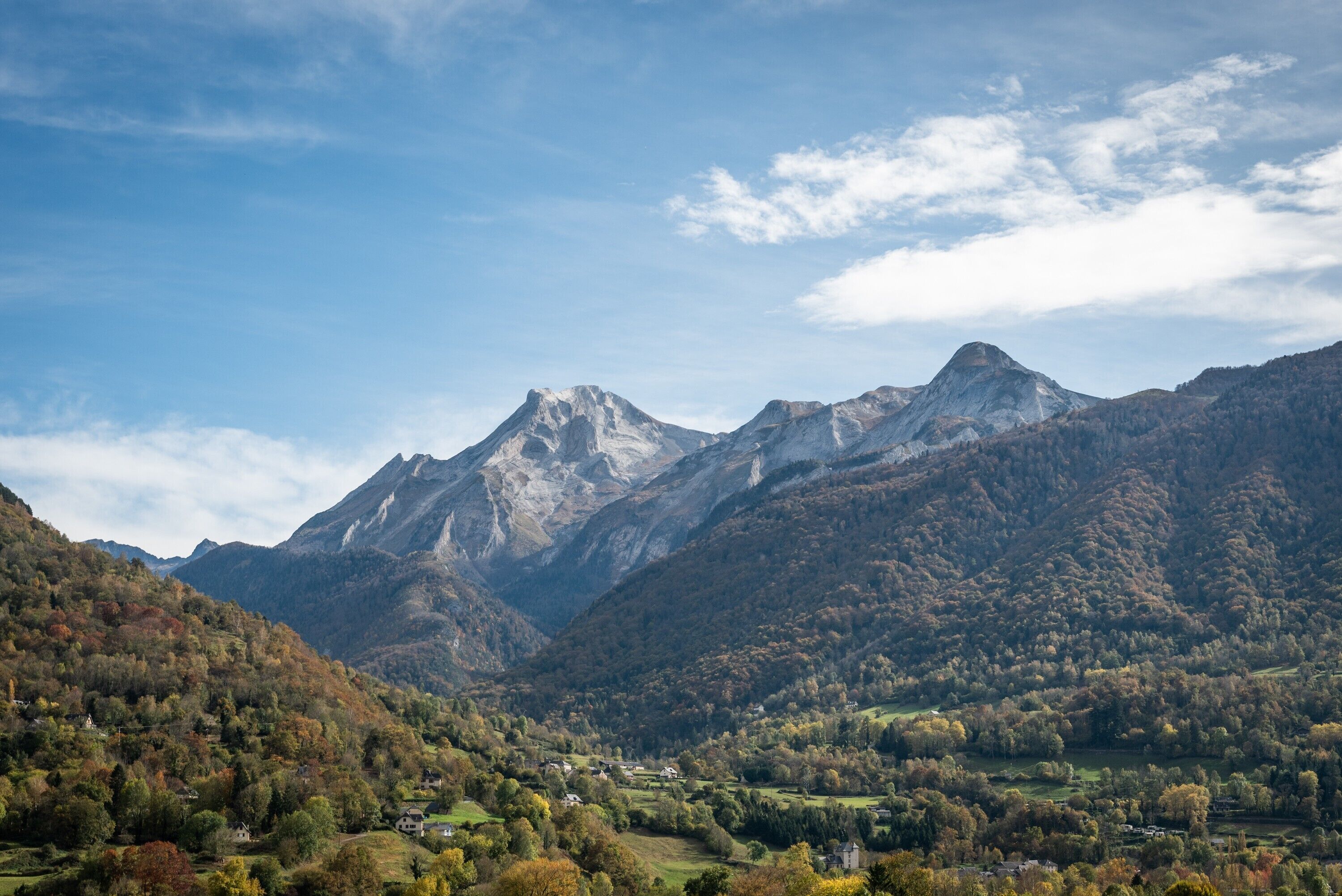 Paisagem montanhosa com um vale, casas e um pico imponente.