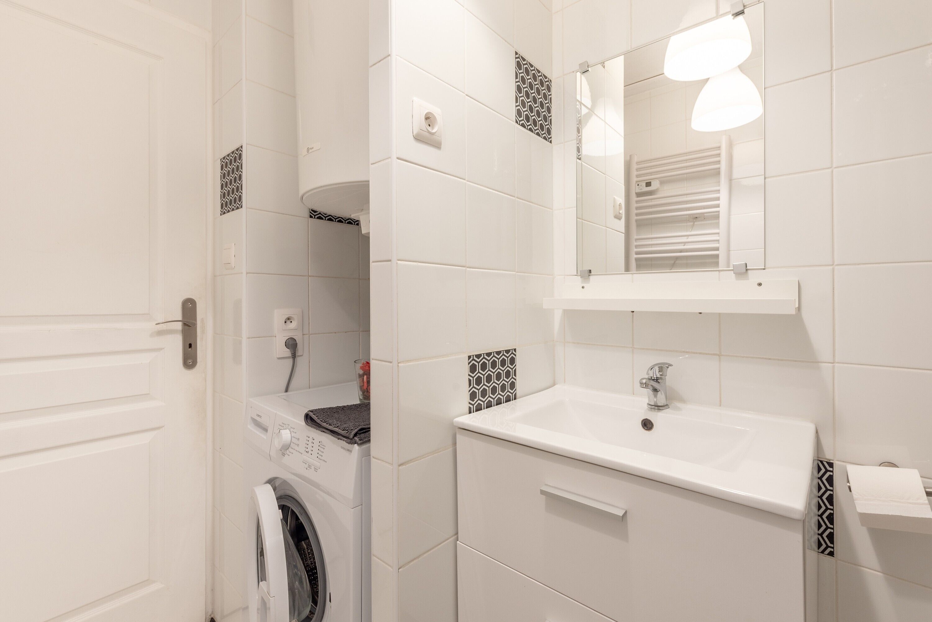 A bathroom with a washing machine, a sink, and a mirror.
