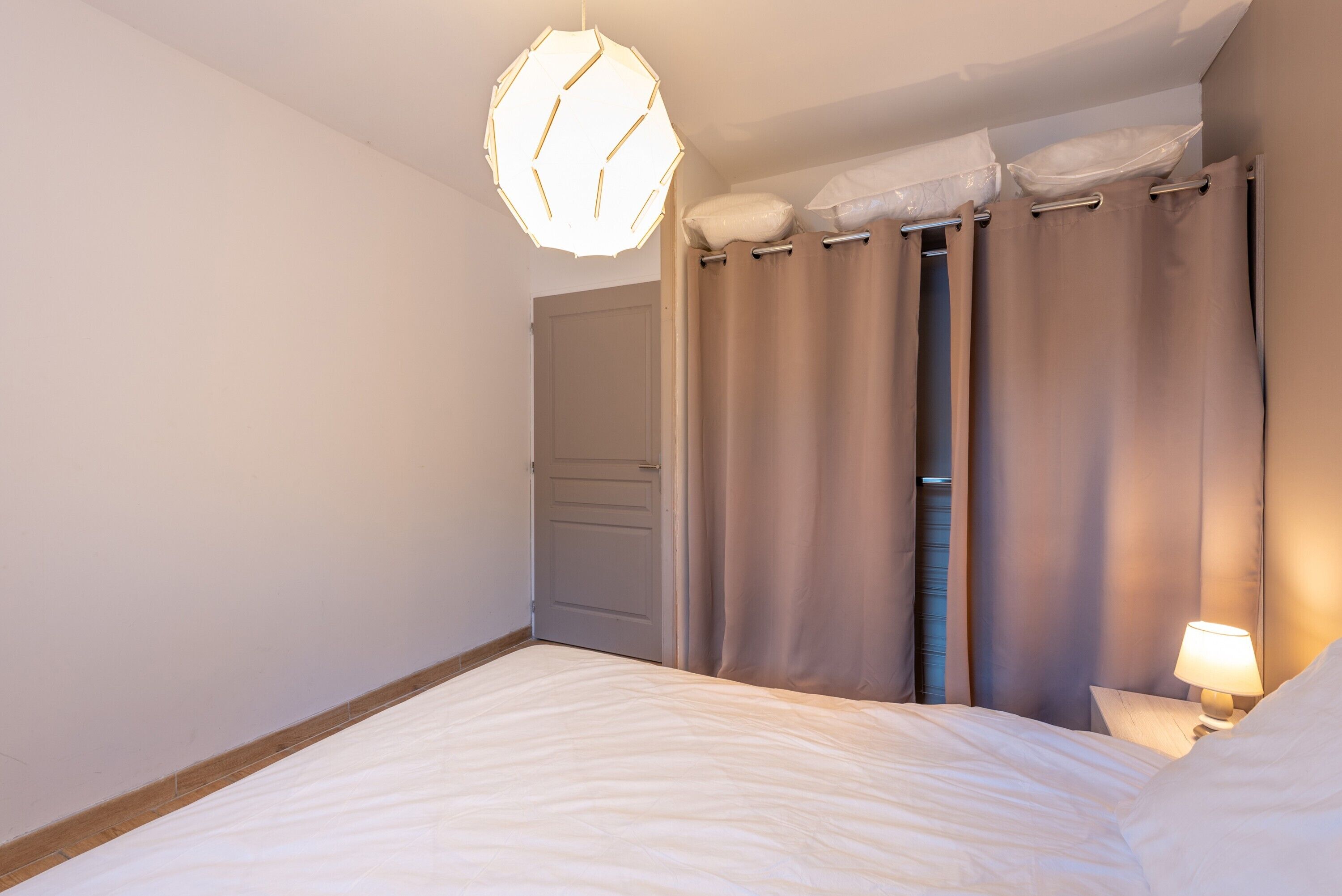 Un dormitorio con cama, lámpara de noche, lámpara colgante y una puerta.