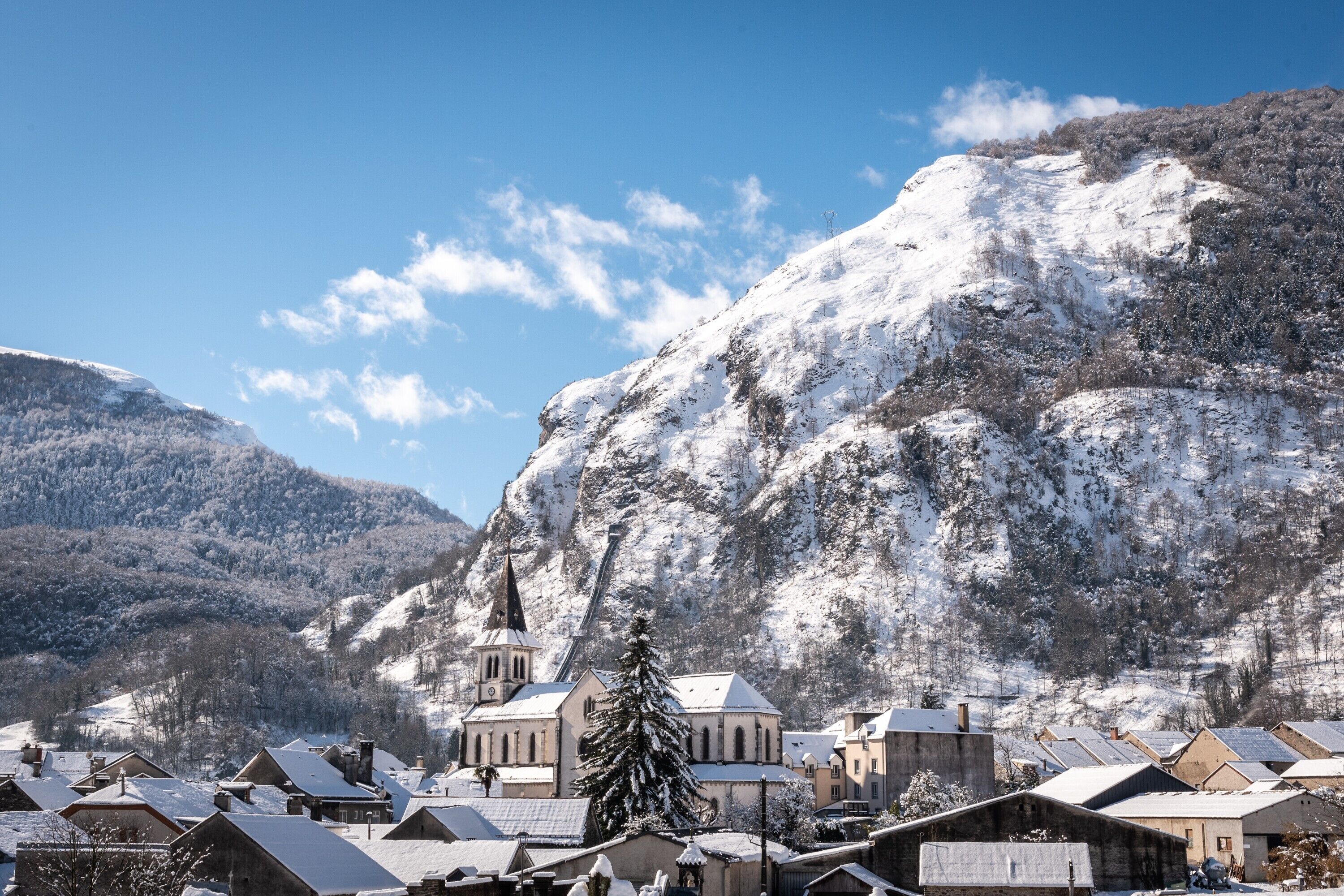 A snow-covered village with traditional buildings, a prominent church, and mountains in the background.