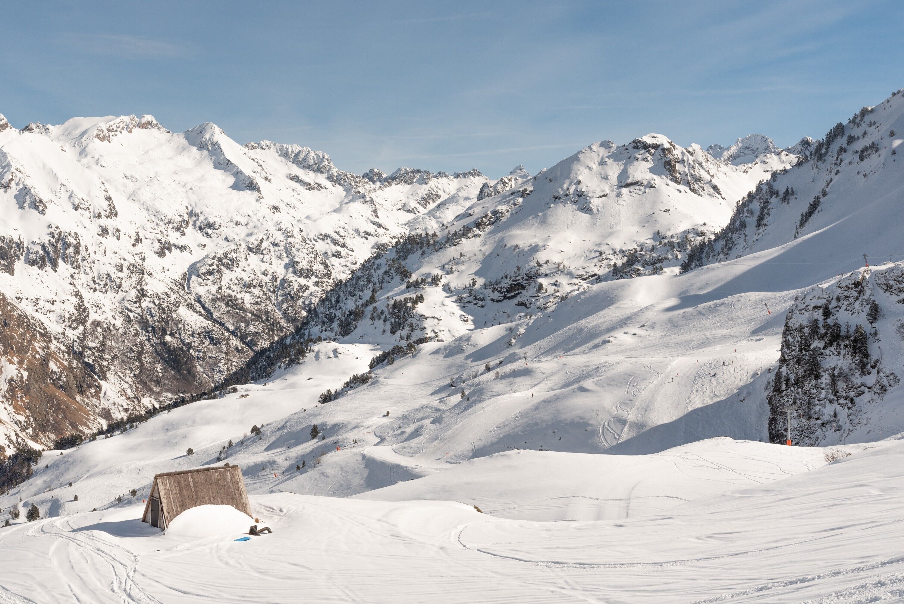 A snow-covered mountain landscape with a wooden structure, likely a ski lodge, and ski tracks.
