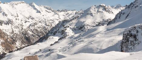 A snow-covered mountain landscape with a wooden structure, likely a ski lodge, and ski tracks.