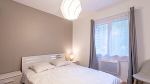 Une chambre à coucher comprenant un lit, une table de chevet, une lampe, une chaise et une fenêtre avec des rideaux.