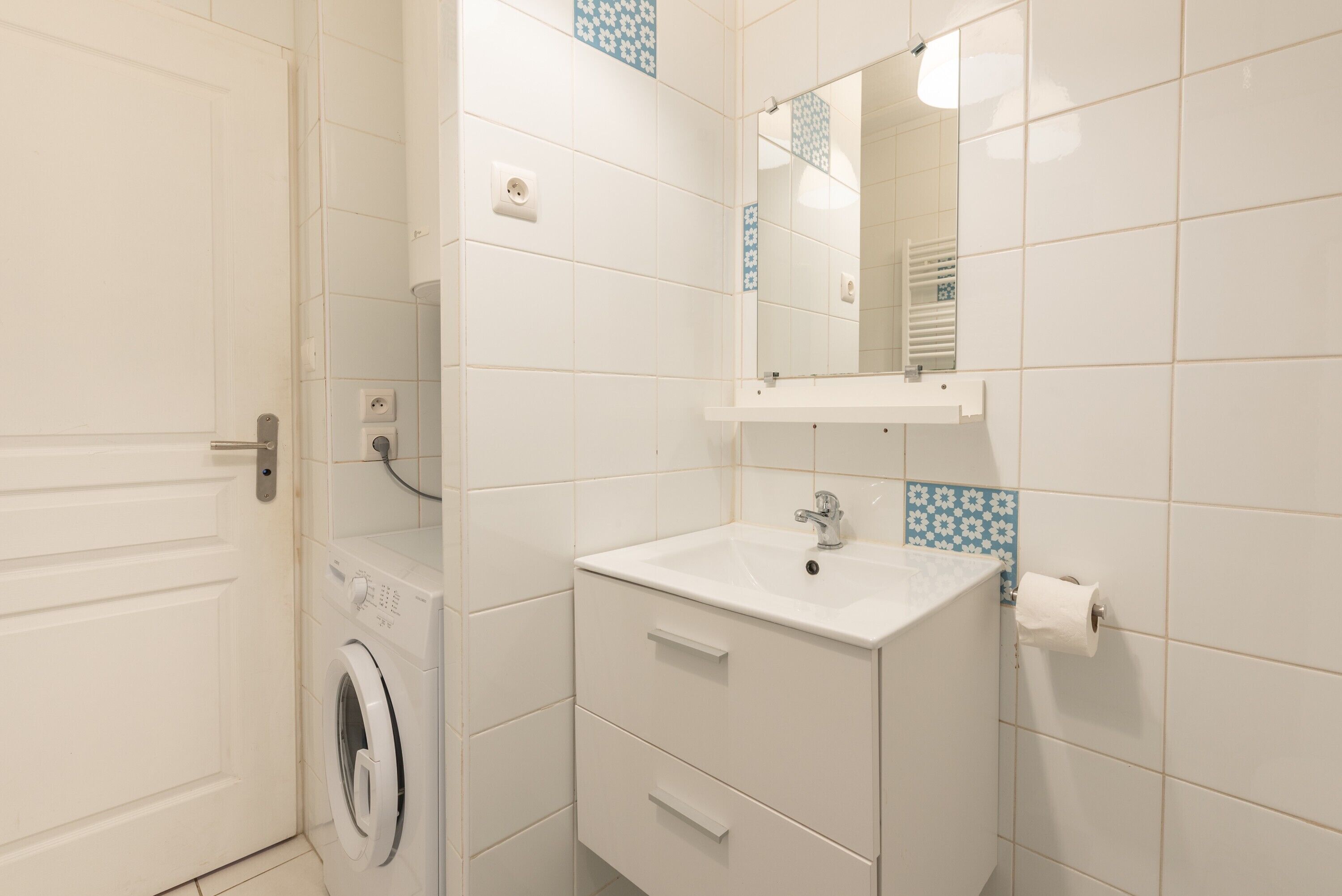 A bathroom with a washing machine, a sink, a mirror, and a towel rack.