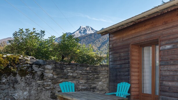 Une cabane en bois avec un mur en pierre, deux chaises turquoise et une table.