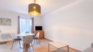 Un salon moderne avec une table à manger ronde, deux chaises, un canapé, un téléviseur et un luminaire décoratif suspendu.