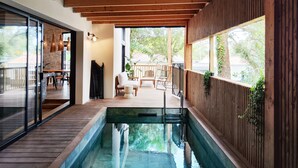 A covered pool area with wooden decking, a seating area with chairs and a table, and a view of the outdoors. - Villa Salicorne 210m2 with swimming pool (Saint-Brevin-les-Pins)