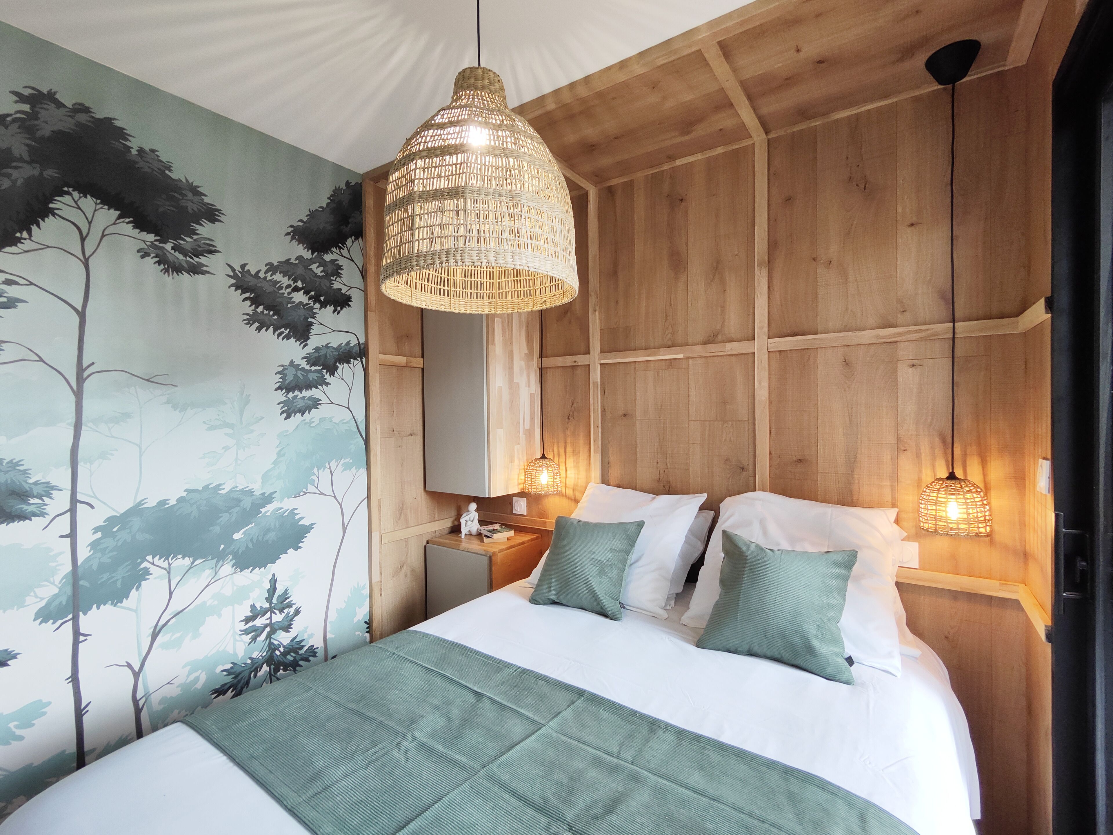 A bedroom with a large bed, two bedside lamps, a wall mural, and a wooden ceiling.