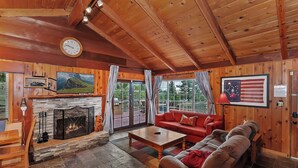 L ’intérieur d’un chalet accueillant, avec une cheminée, des murs en bois, un canapé rouge et une grande fenêtre avec des rideaux.