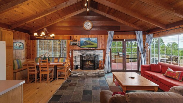 L’intérieur chaleureux d’un chalet avec une cheminée en pierre, des meubles en bois et de grandes fenêtres donnant sur le paysage extérieur.