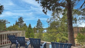 Une terrasse avec quatre chaises bleues et une balustrade blanche, donnant sur une zone boisée avec un lac et un bâtiment en arrière-plan.