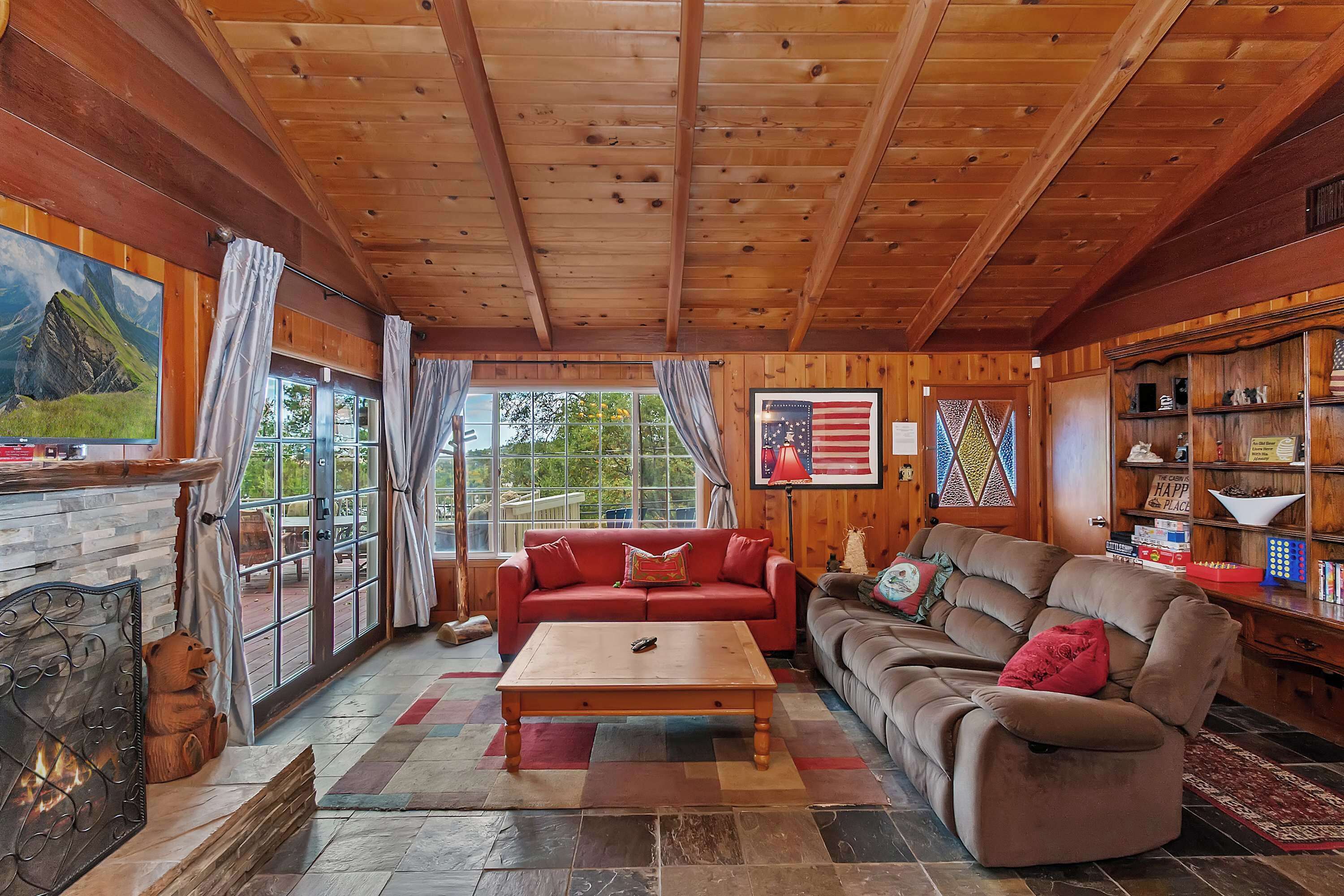 A cozy living room with a fireplace, wooden ceiling, large windows, and a comfortable sofa.