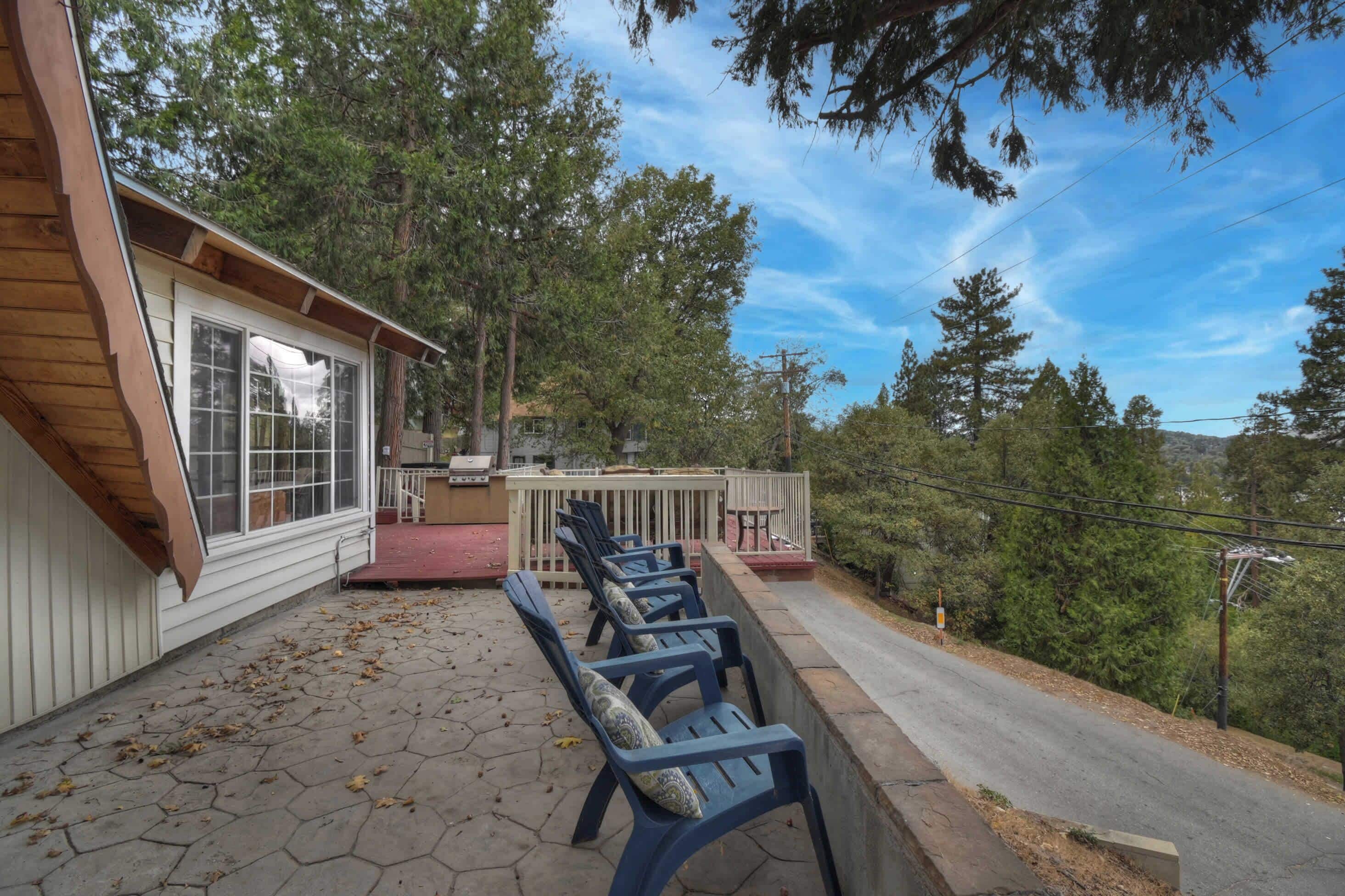 A covered patio with blue chairs, a wooden deck, and a view of trees and hills.