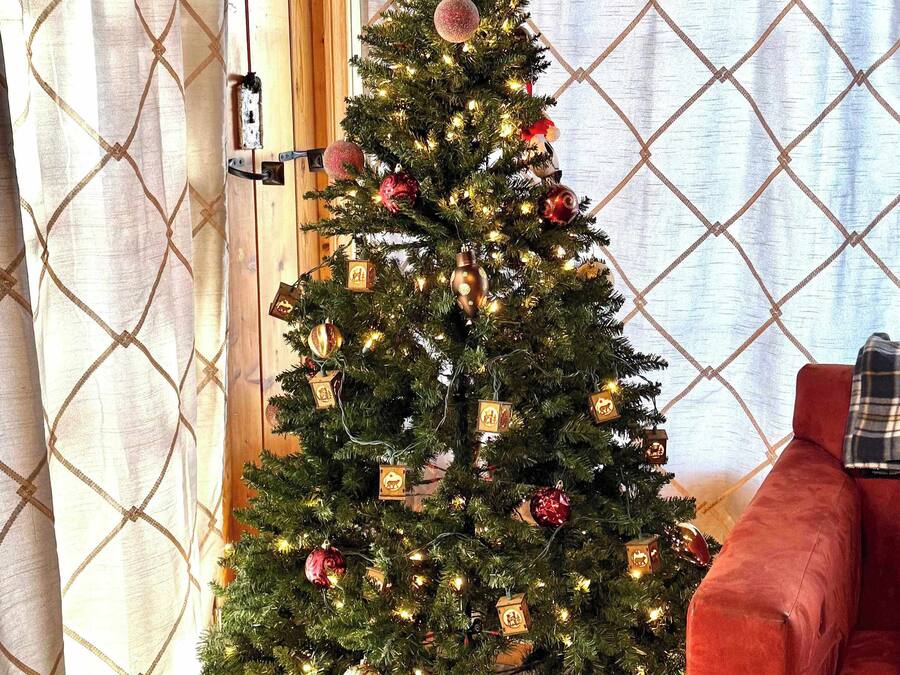 A Christmas tree with ornaments and lights in a room with a red couch and patterned curtains.