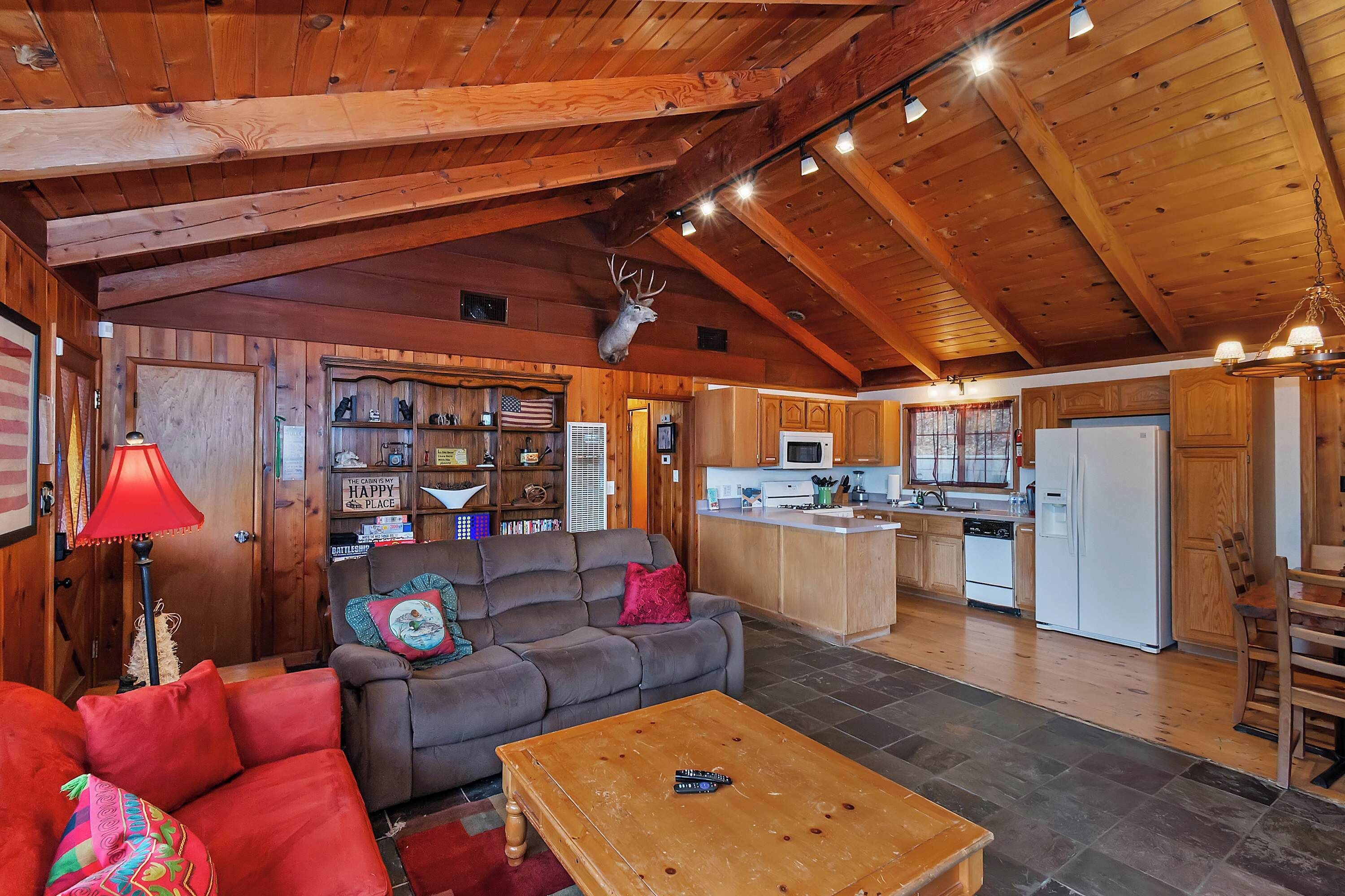 Interior de una cabaña con sala de estar, cocina y un venado montado en la pared.
