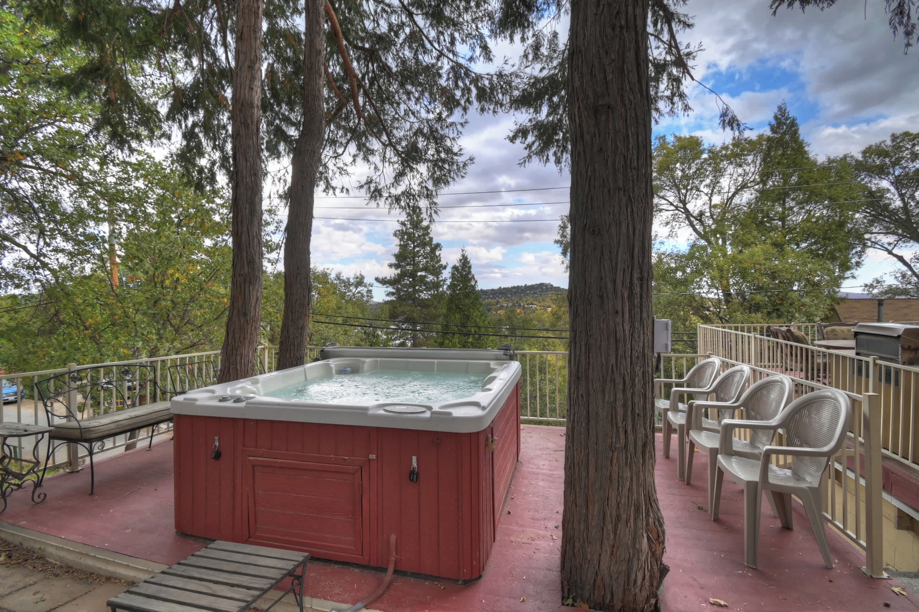 A hot tub on a deck with chairs, surrounded by trees and a view of a hill.