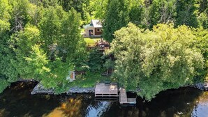 A house surrounded by dense green trees, a dock, and a small bridge.