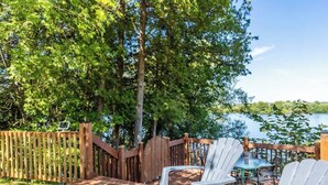 A wooden deck with white chairs and a table, overlooking a lake.