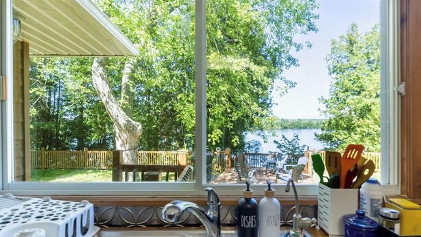 A kitchen with a large window overlooking a backyard with a wooden deck and trees.