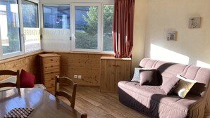 Une pièce chaleureuse avec une table en bois, des chaises, un canapé confortable et une fenêtre donnant sur un paysage verdoyant.