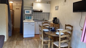 Une cuisine compacte équipée d’un four à micro-ondes, d’un grille-pain et d’une machine à café. On y trouve une table à manger avec des chaises, ainsi qu’un téléviseur fixé au mur.