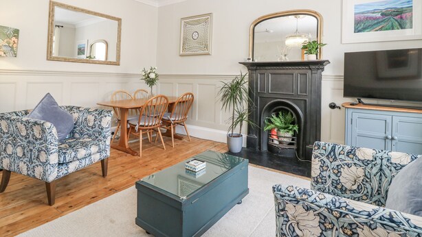 A living room with a fireplace, a dining table with chairs, a television, and floral-patterned furniture.