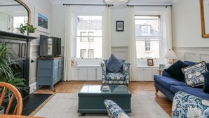 A living room with a sofa, armchair, and coffee table, a television on a cabinet, and a chandelier.