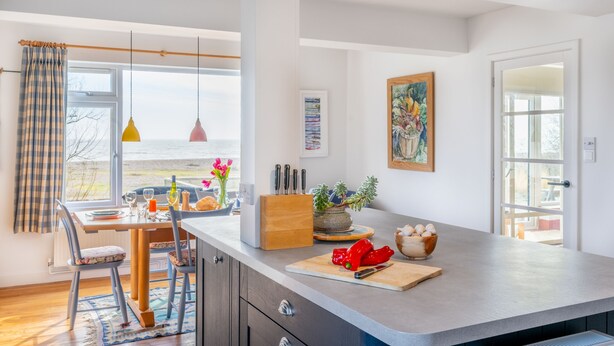 A modern kitchen with a large island, a dining area with a view, and a window with curtains. - Chicoutimi 4, Thorpeness (Thorpeness)
