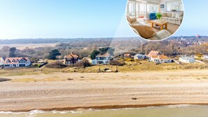 A coastal property with a view of the sea, a large living room with a sofa and coffee table, and a dining area with a table and chairs. - Chicoutimi 4, Thorpeness (Thorpeness)