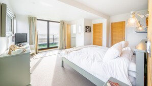 A modern hotel room with a large bed, a desk with a television, and a view of the city through the window. - Chicoutimi 4, Thorpeness (Thorpeness)