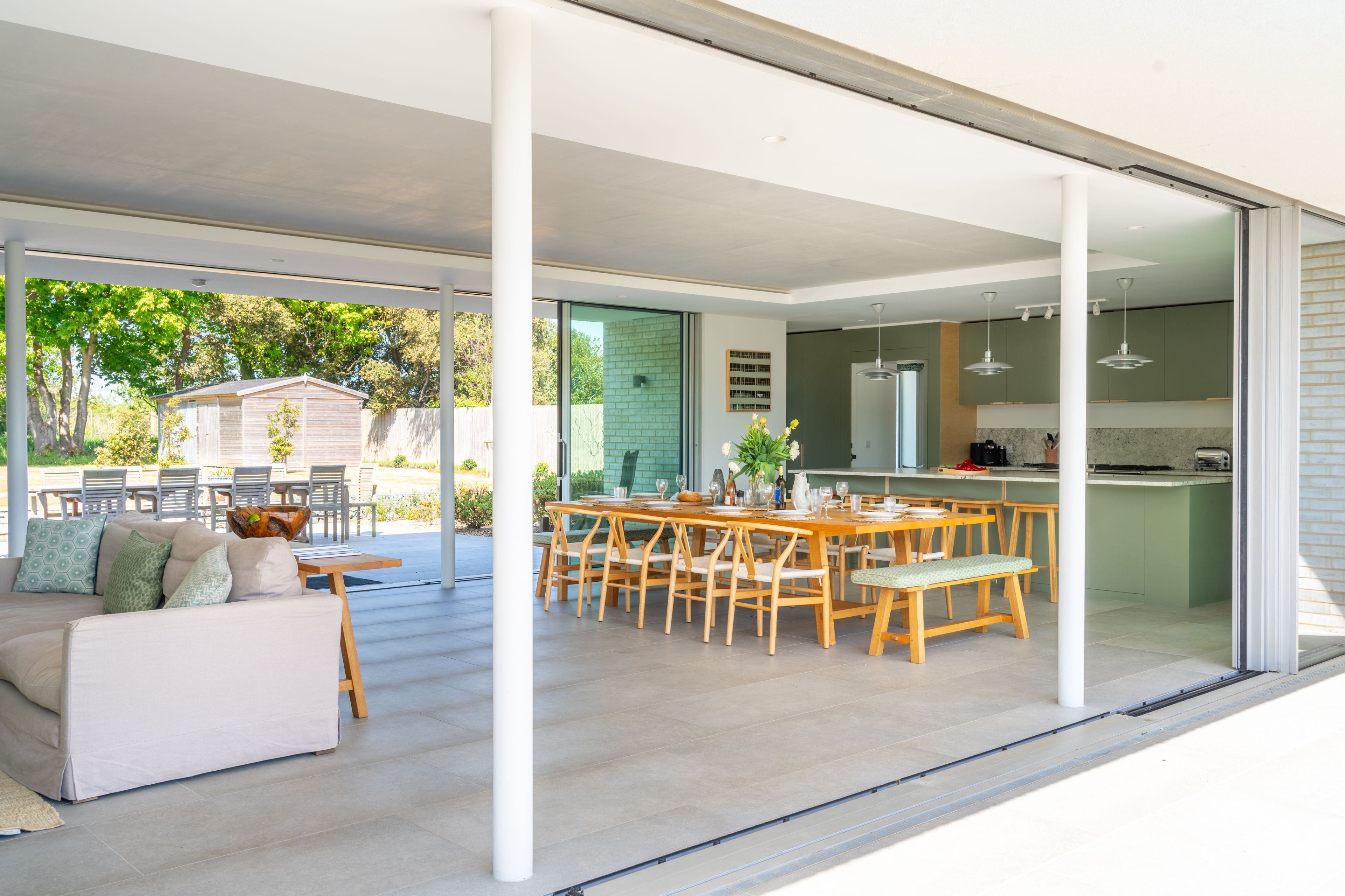 An open-plan living area with a dining table and chairs, a sofa, and a kitchen visible through glass doors.