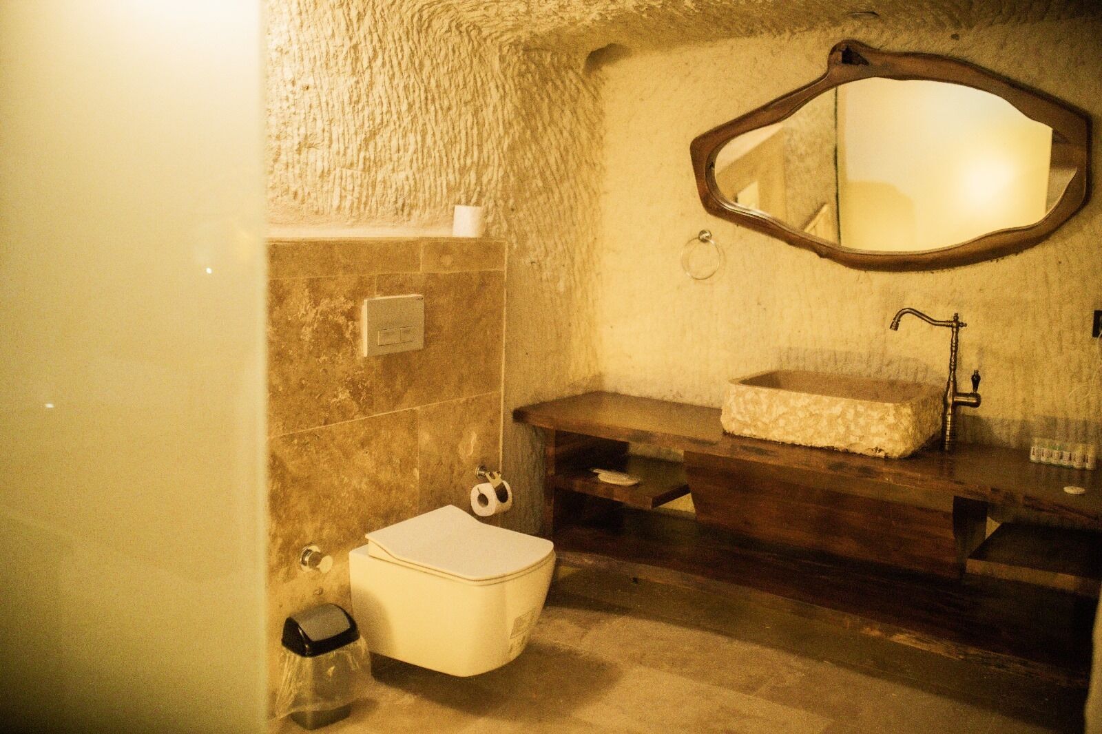 A bathroom with a toilet, sink, mirror, and a textured wall.