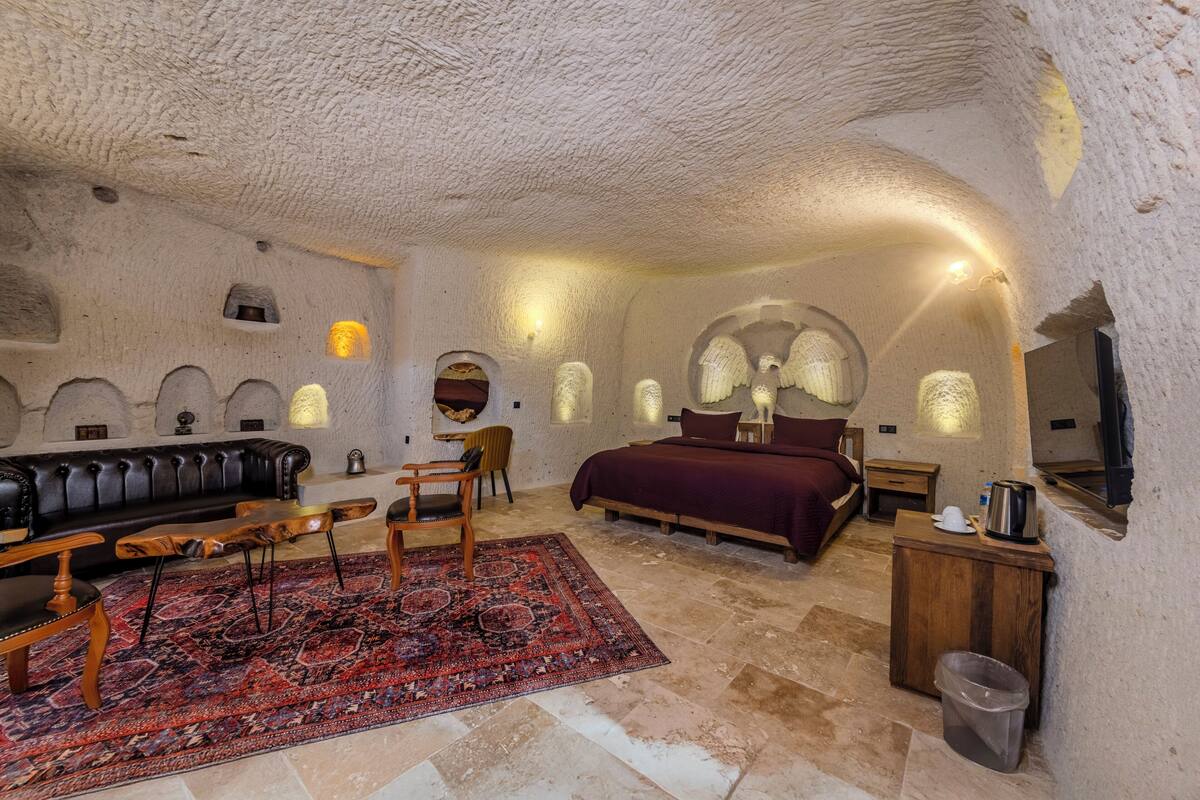 Ein gemütlicher, rustikaler Raum mit Ledersofa, Holztisch und einem großen Bett mit roter Bettdecke.