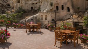 A terrace with wooden tables and chairs, potted plants, and a view of ancient rock formations. - Rose Moon Cave (Nevşehir)