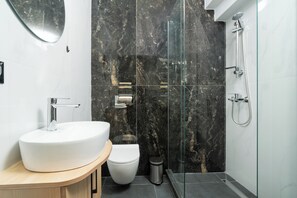 A modern bathroom with a white sink, a toilet, and a glass-enclosed shower area. - TOWER 15 Suites (Thessaloniki)