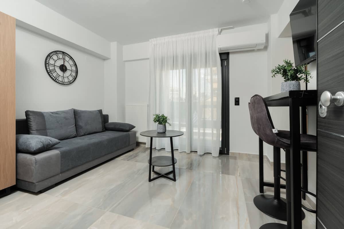 A modern living room with a grey sofa, a round table with a plant, and a black chair.