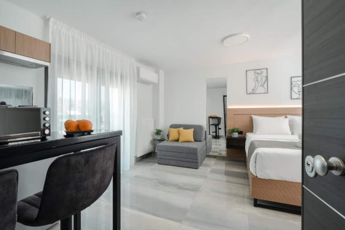 A modern hotel room with a bed, a desk with a chair, a small sofa, and a dining table.