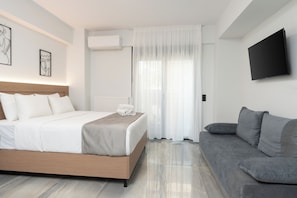 Una habitación de hotel moderna con una cama, un sofá gris, un televisor de pantalla plana y obras de arte en las paredes.