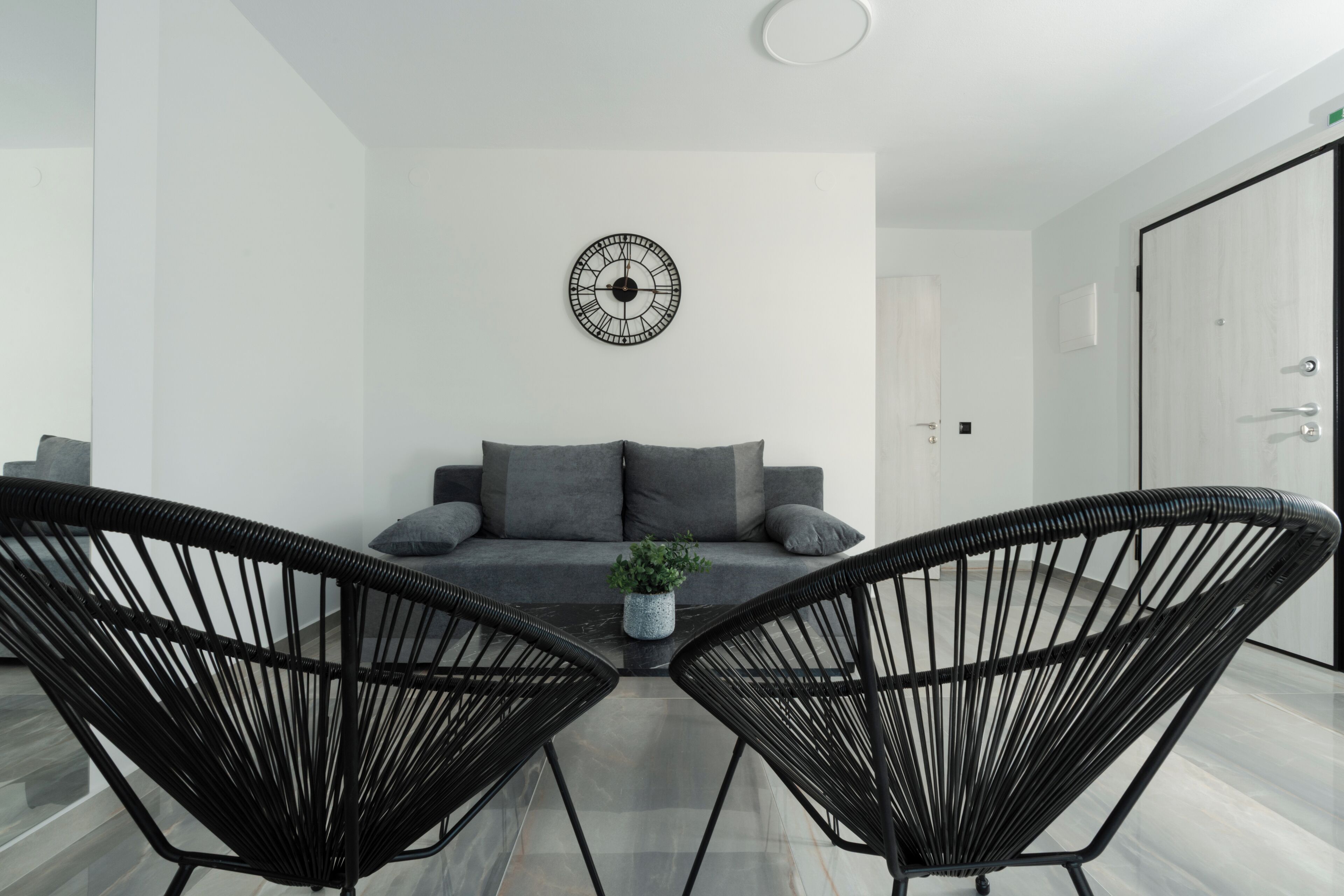 Ein modernes Wohnzimmer mit einer Couch, zwei schwarzen Sesseln, einem Couchtisch und einer Wanduhr.