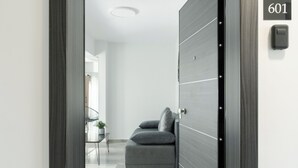 A modern interior with a dark wooden door, a visible room number 601, and a glimpse of a living area with a sofa and a small table. - TOWER 15 Suites (Thessaloniki)