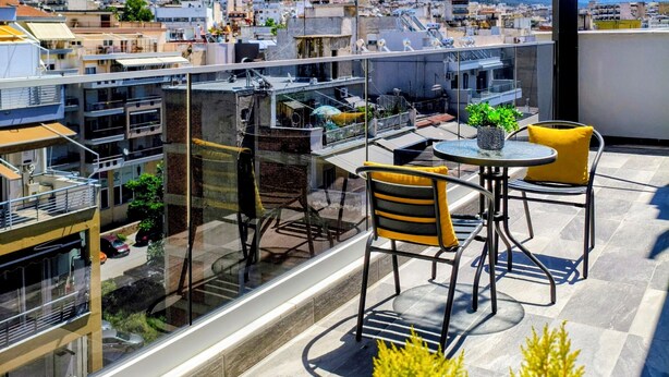 A rooftop terrace with a table and chairs, a potted plant, and a view of the cityscape and mountains. - TOWER 15 Suites (Thessaloniki)