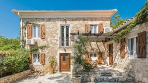 A stone building with wooden shutters, a balcony, and a paved courtyard.