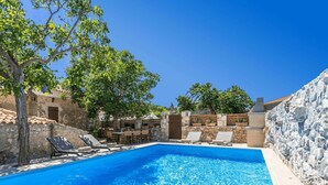 A swimming pool with lounge chairs, a stone wall, and a tree.